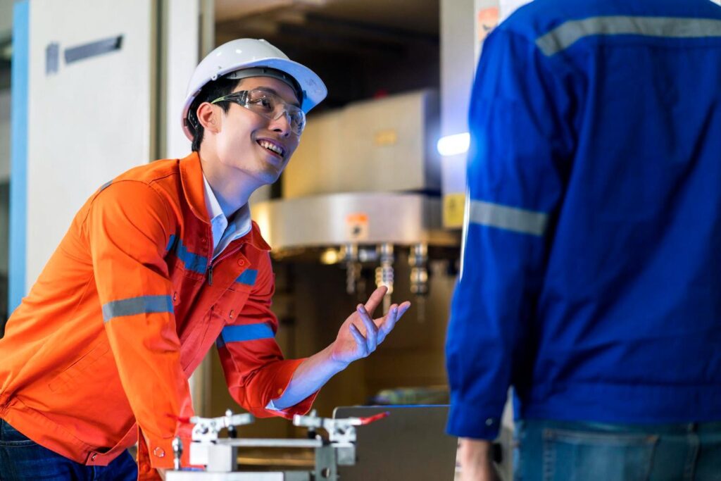 An engineer in an orange safety uniform is discussing machinery with a coworker.