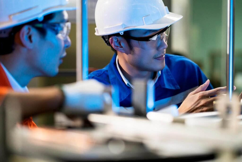 Engineers in safety helmets inspecting machinery inside an industrial facility.