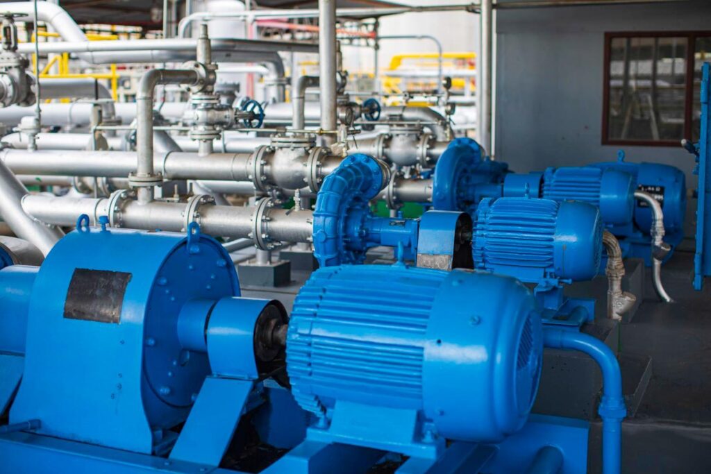 Blue industrial pumps connected to metal piping inside a processing plant.