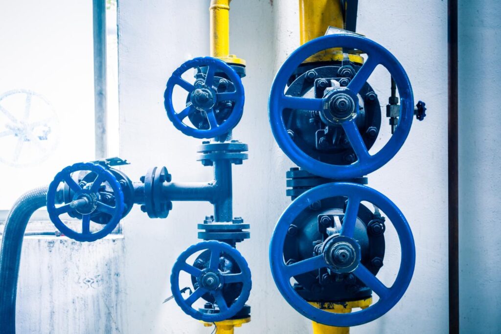 Blue handwheel-operated valves installed on yellow-painted process piping at an industrial plant.