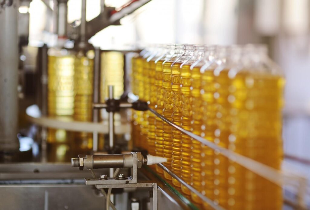 Bottles of golden palm oil on a filling line at a palm oil processing and packaging plant.